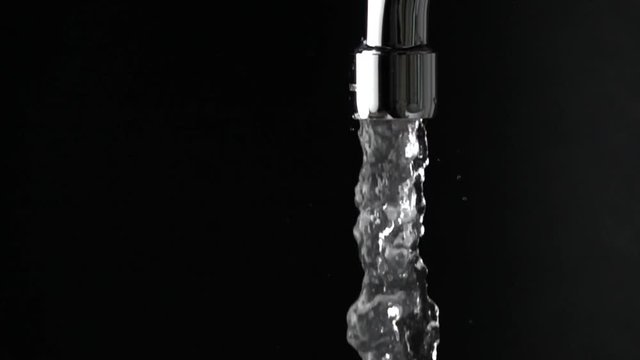 Close up slow motion shot of water running from tap against black background