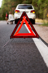 Red warning triangle and broken car in the middle of forrest