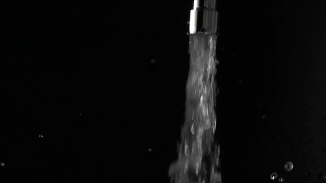 Super slow motion shot of water running from tap and splashes, black background