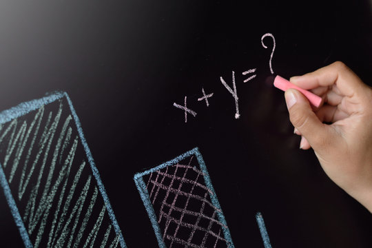 Business woman is drawing charts, plans, diagrams mathematical equation with two unknowns and question mark by colored chalk on a blackboard