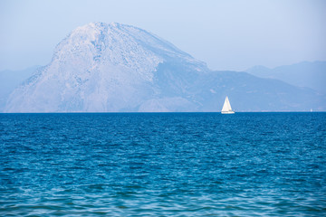 White sailboat in the blue sea with mountains - Powered by Adobe