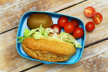 Healthy lunch box containing whole grain cheese sandwich, kiwi fruit and cherry tomatoes on rustic wooden surface
