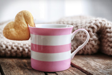 Heart shape cookie on cup of coffee on wooden table closeup