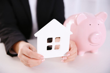 Savings concept. Woman holding piggy bank in one hand and house figure in another, close up