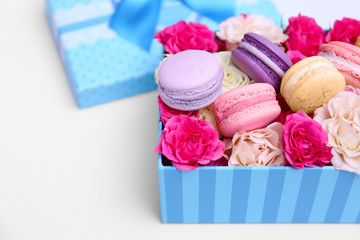 Tasty macaroons and roses in box on white background