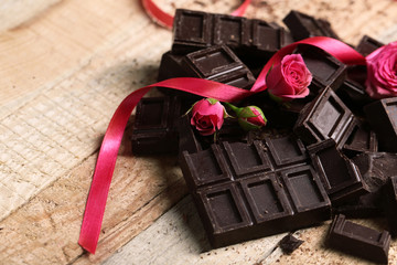 Chocolate pieces and roses on wooden background