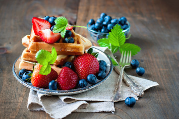 Belgian waffles with strawberries, blueberries and syrup, homemade healthy breakfast, toned image selective focus