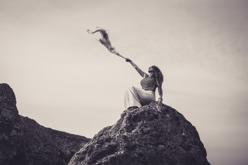 Beautiful woman sat on top of cliff holding scarf to wind
