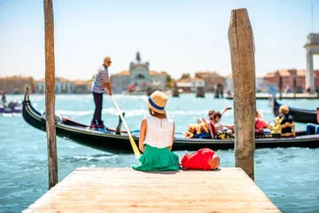 Fototapete Gondeln Junge Reisende, die auf dem Pier sitzen und eine schöne Aussicht auf den venezianischen Kanal mit Gondeln genießen, die in Venedig schwimmen?