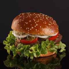 Juicy, tasty burger with pickles, tomatoes and onions on a black background