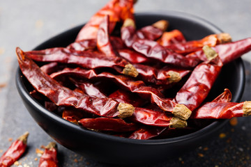Dried red chili peppers in bowl on slate background