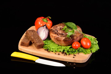 Tasty meat medallion, lettuce, onion, pepper, tomatoes and slices of bread on a wooden cutting board alongside with ceramic knife
