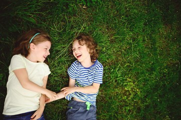 Two cheerful children lie on a green grass.