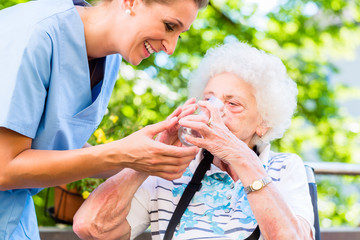 Altenpflegerin gibt Seniorin Glas Wasser zu trinken