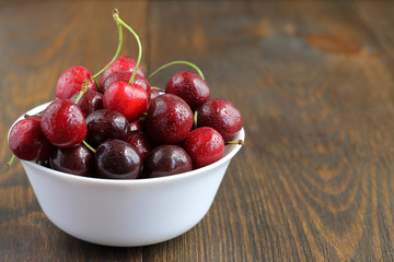 Sweet cherries in bowl on wooden background.