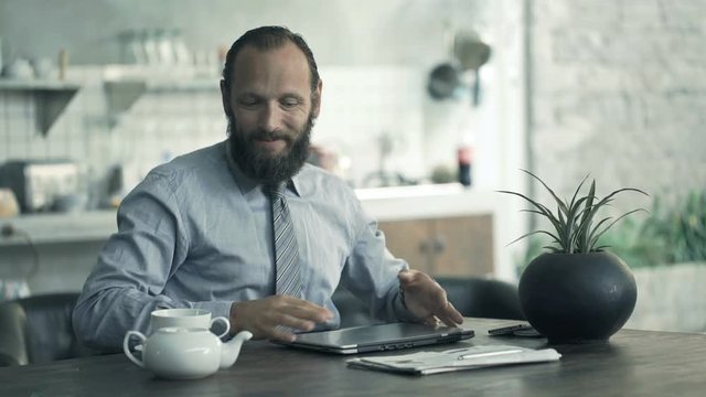 Businessman finishing working on laptop and drinking tea by table at home
