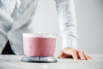 Man pours some organic honey inside blender pot with freshly made cold berry smoothie, preparation process in cafe