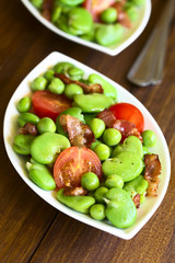 Broad bean, green pea, cherry tomato and fried bacon salad, photographed on dark wood with natural light (Selective Focus, Focus one third into the image)