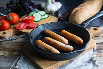 Frying pan with fried sausage and vegetables on a wooden table.