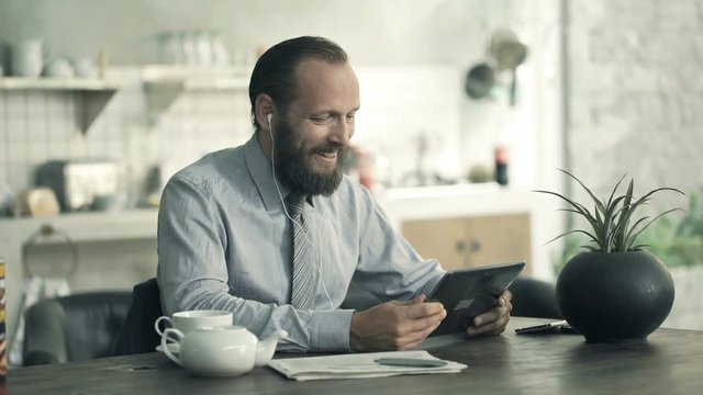 Young, happy businessman watching movie on tablet in kitchen at home
