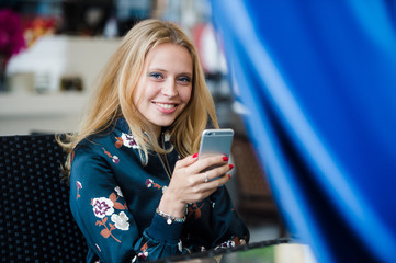 Attractive woman in street cafe reading a text message from her phone and smiling