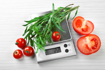 Tomatoes and tarragon with digital kitchen scales on wooden background