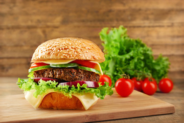 Big hamburger with vegetables on wooden background