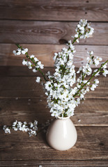 Vintage vase with cherry flowers on old wooden background.