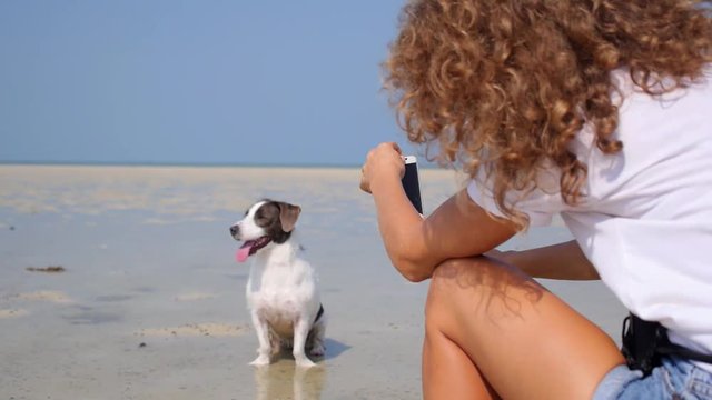 Young Woman Photographing Her Dog on Beach with Cellphone
