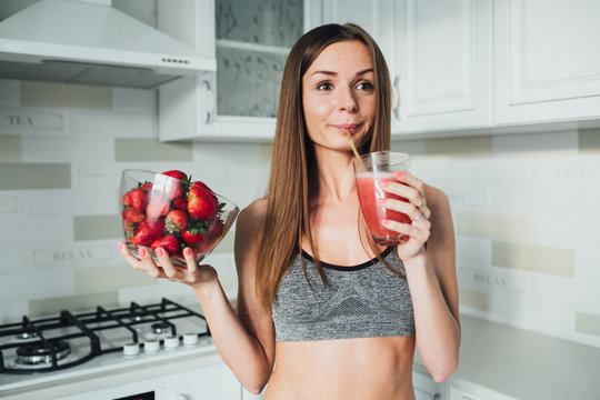 Sports and sexy girl drinks strawberry smoothie in the kitchen