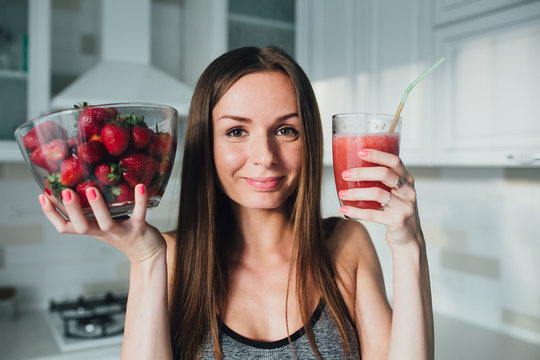 Sports and sexy girl drinks strawberry smoothie in the kitchen