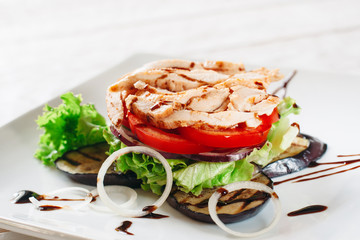 Chicken with grilled eggplant and tomato layered. Close-up of portion of layered meal of fried chicken, tomato, onion, lettuce and grilled eggplant, decorated with chocolate sauce