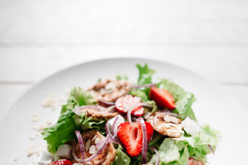 Strawberry and chicken steaks mix with onion copyspace. Top view on plate with mix of grilled chicken steaks, strawberries, onion and mozzarella cheese on white wooden background.