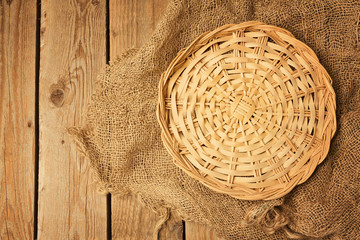 Empty wicker basket on sackcloth on wooden table background. View from above