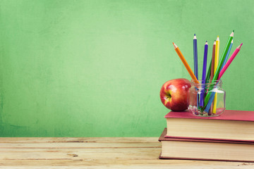 Back to school background with books, color pencils and apple over green wallpaper