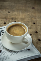 A newspaper and a cup of coffee on a wooden table