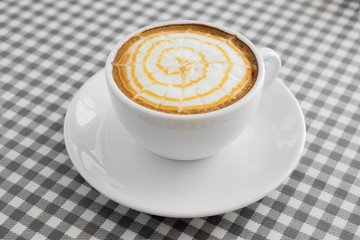 Cup of hot Cappuccino Coffee with Latte Art on plaid table cover