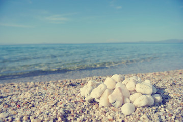 Heap of white pebbles on the beach, on a sunny day, with blue sea in the background. Image filtered in faded, washed-out, retro, Instagram style; nostalgic concept of summer holidays. - 113282008