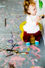Naklejka premium beautiful little girl draws on the wall with paints, brushes for painting, freehand drawing