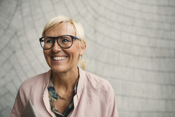 Happy businesswoman wearing eyeglasses against wall