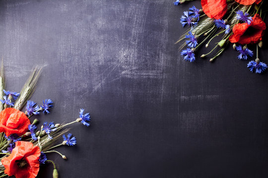 Red poppies with blue cornflowers and rye on old blackboard with