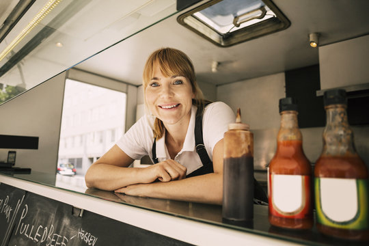 Portrait of happy female chef leaning on counter at food truck