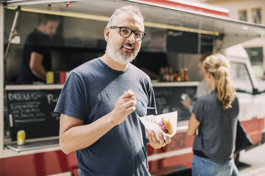 Portrait of mature man with food standing against truck at street