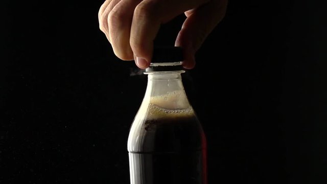 Man opens cola plastic bottle with screw top. Slow motion shot, black background