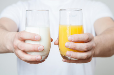 Male hands holding a glass of orange juice and a glass of milk