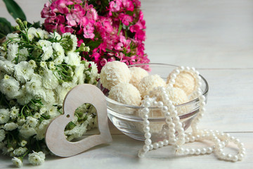 full a glass bowl with beads and decorative heart on wooden background near the pile of flowers
