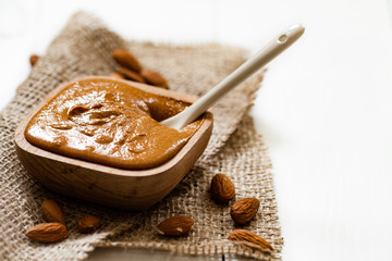 Homemade almond butter in a wooden bowl and a bag of jute.