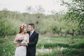 Beautiful bride in a wedding dress with bouquet and roses wreath posing with groom wearing wedding suit. Wedding day