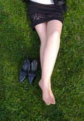 Young business woman took her high heels off to rest the feet  and sits on a grass in park