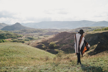 Fototapeta na wymiar Young beautiful woman traveler wearing hat and poncho relaxing on the top of the hill with mountains and hills around